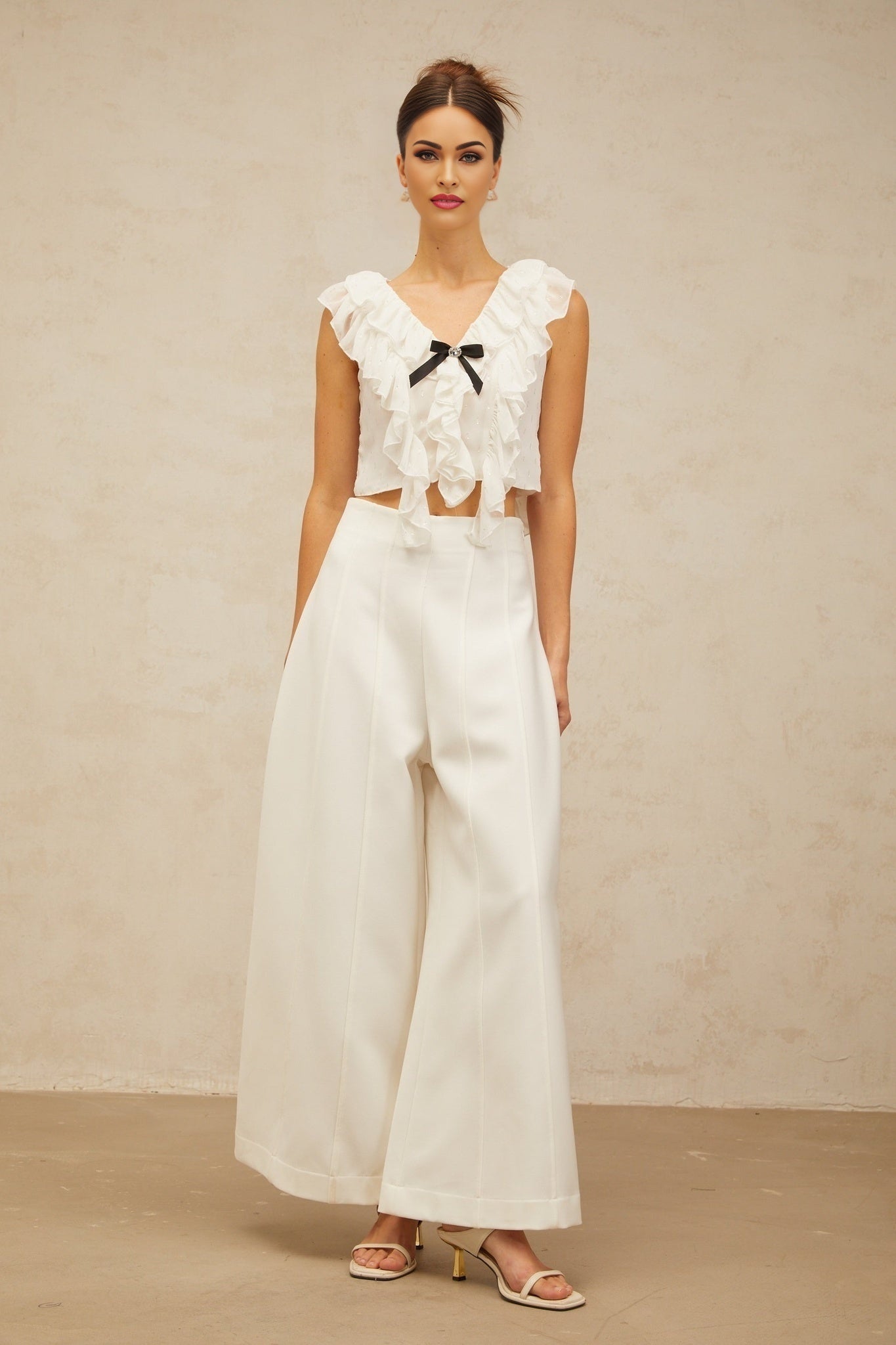 Woman wearing white sleeveless cropped top with ruffled chiffon fabric and bow detail at neckline