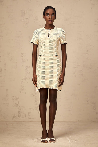 Woman wearing a short beige knitted dress with ruffled details and a delicate pointelle pattern