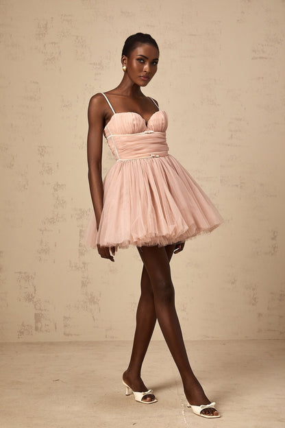 Young woman wearing a short sleeveless dress with a pleated tulle skirt in a light color against a plain background