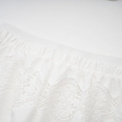A woman wearing a white lace trimmed cropped top and matching trousers The top features cutout details and the set has a delicate feminine design