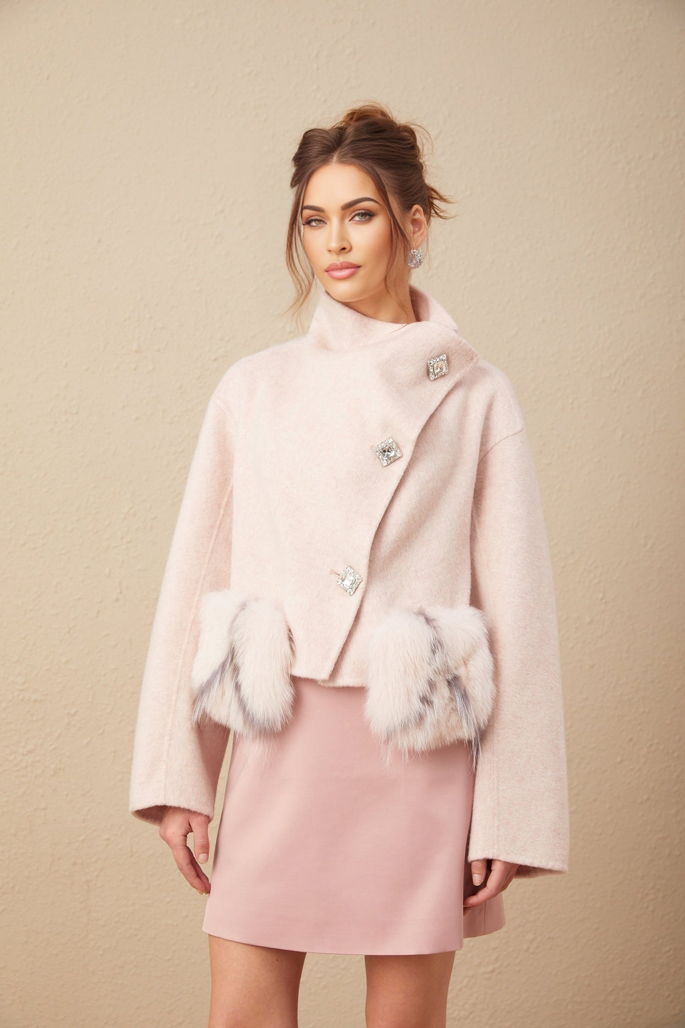 Woman wearing a short pink coat with diagonal button placket standing against a plain background