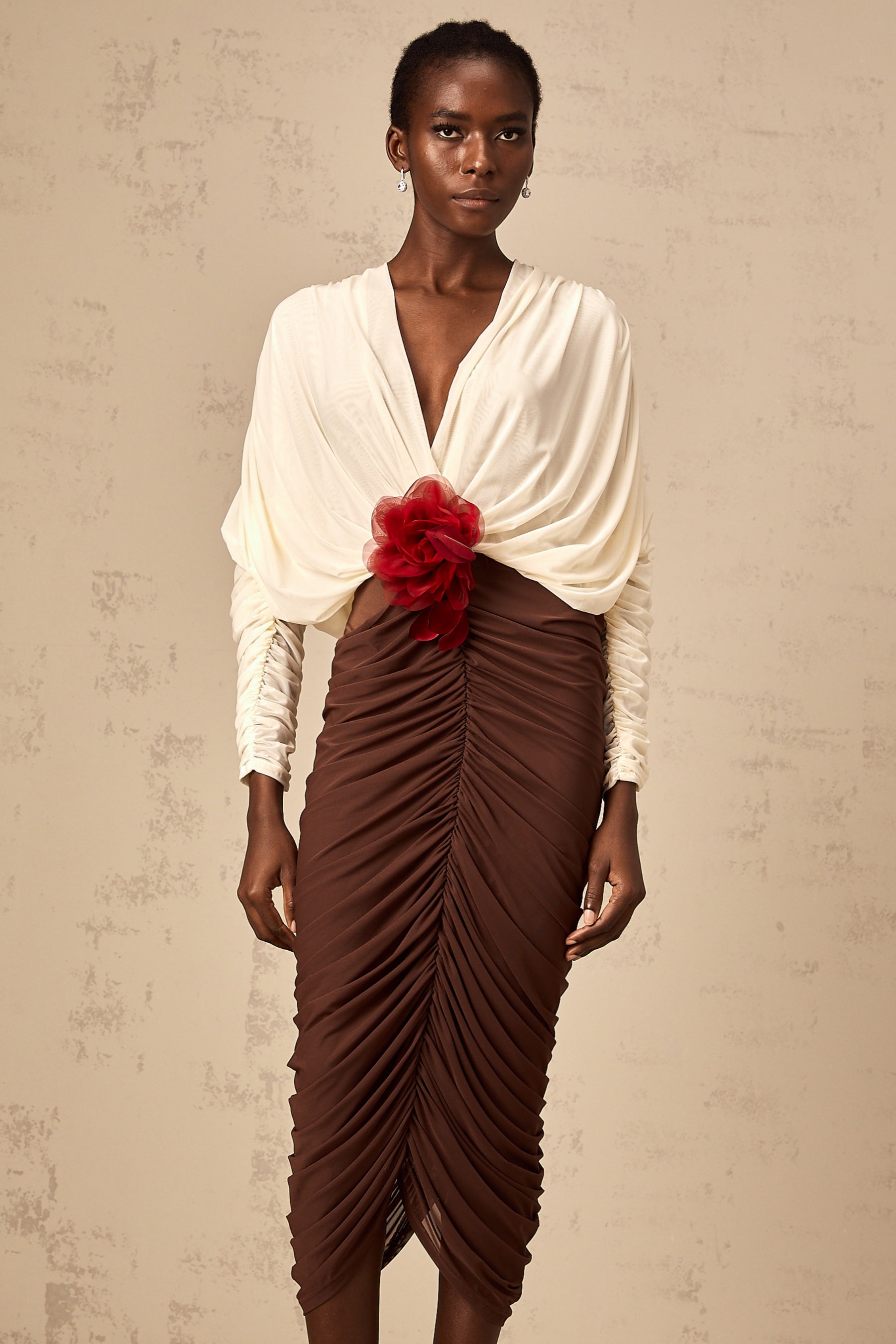 A woman wearing a colorblocked midi dress with ruched detailing and a flower brooch accent The dress features contrasting colors and falls to mid calf length
