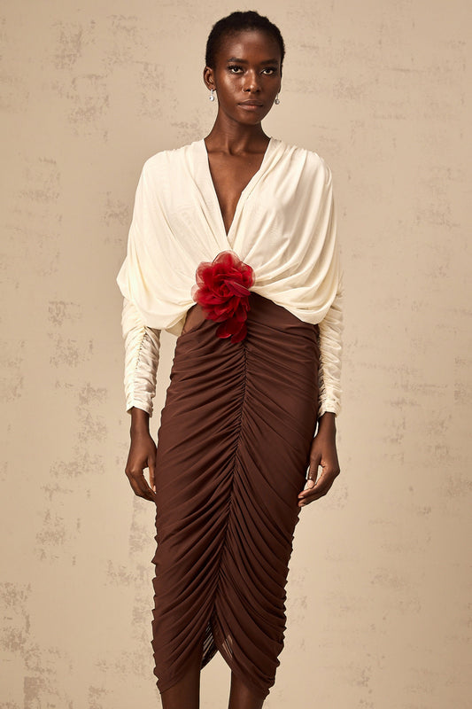 A woman wearing a colorblocked midi dress with ruched detailing and a flower brooch accent The dress features contrasting colors and falls to mid calf length