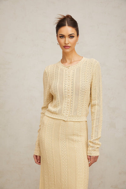 A woman wearing a matching white pointelle knit cardigan and skirt set The cardigan has long sleeves and an open front The skirt is knee length The set has a delicate lacy pattern throughout