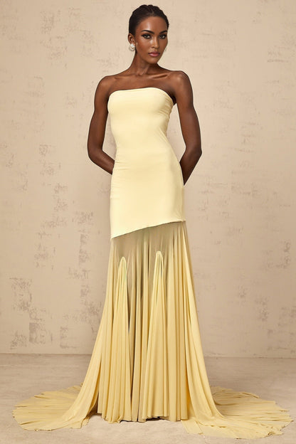 A yellow offshoulder maxi dress with sheer tulle fabric flowing to the floor worn by a model against a plain background