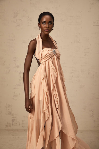 Woman wearing a long pink chiffon maxi dress with ruffle details and halter neck style