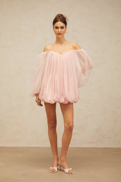 Young woman wearing a pink layered bubble tulle mini dress with a fitted bodice and voluminous skirt standing against a plain background