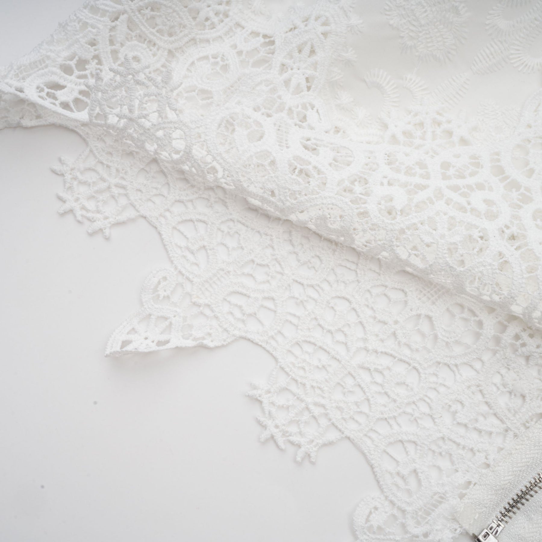 Woman wearing matching white lace trimmed cropped top and trousers set with cutout details