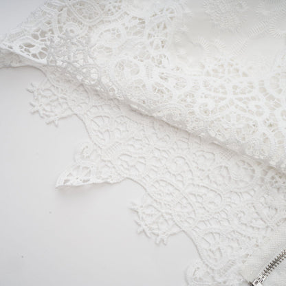 Woman wearing matching white lace trimmed cropped top and trousers set with cutout details