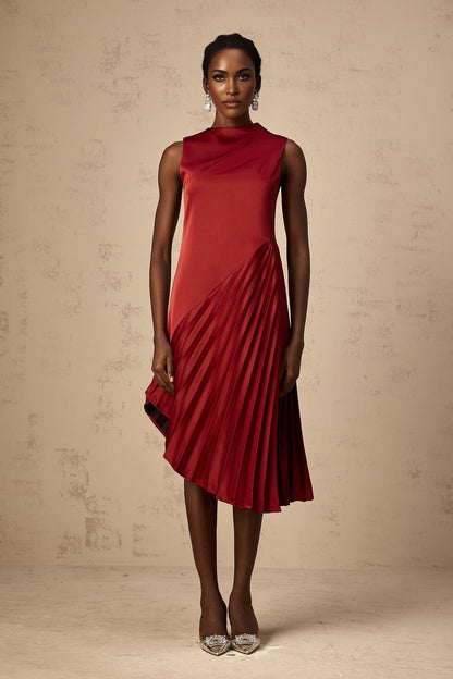 A woman wearing a wine red midi dress with an asymmetric neckline and pleated skirt standing against a plain background