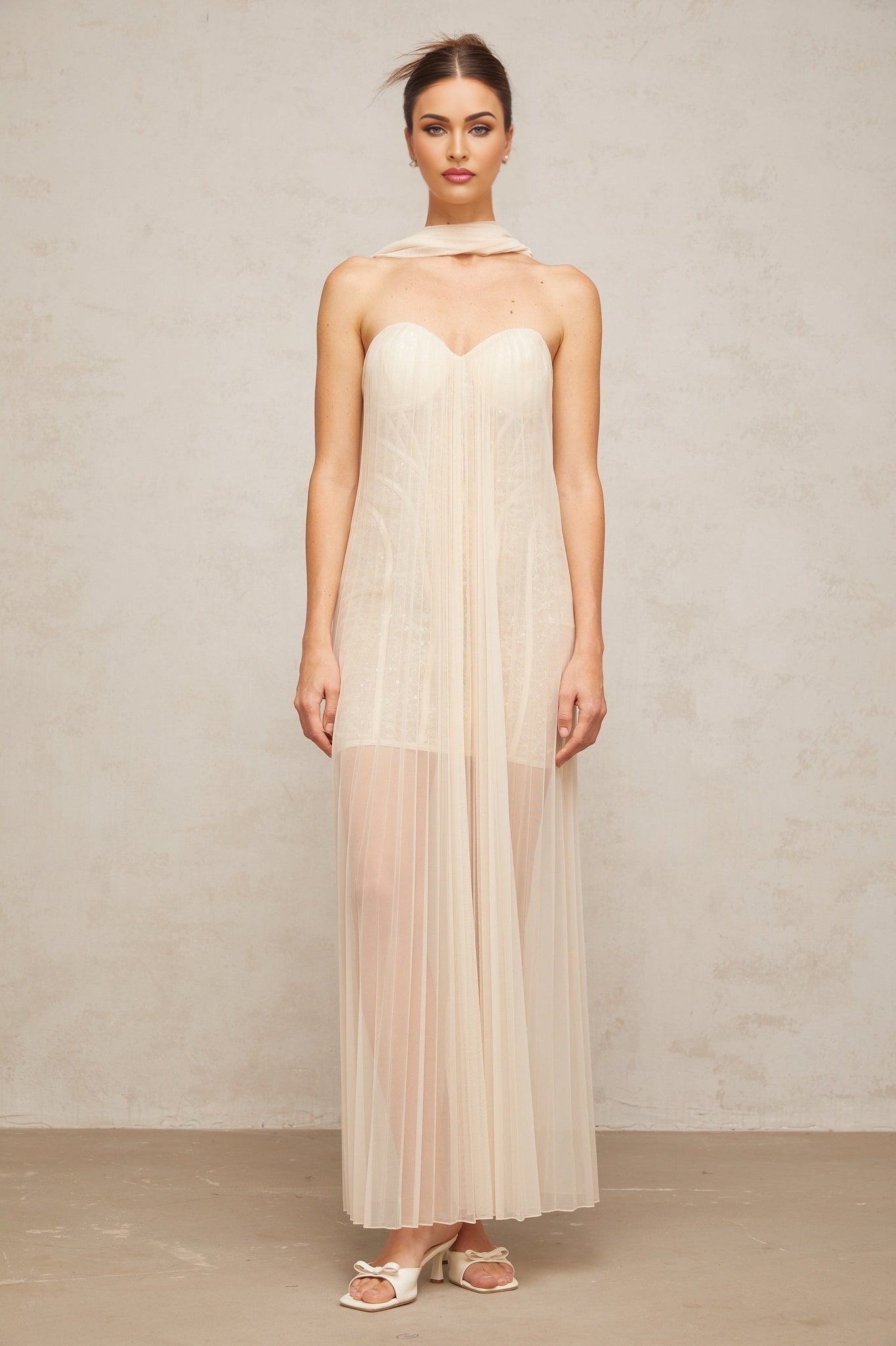 Woman wearing long neutral colored tulle maxi dress with ribbon design and pleated details