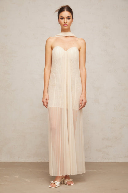 Woman wearing long neutral colored tulle maxi dress with ribbon design and pleated details
