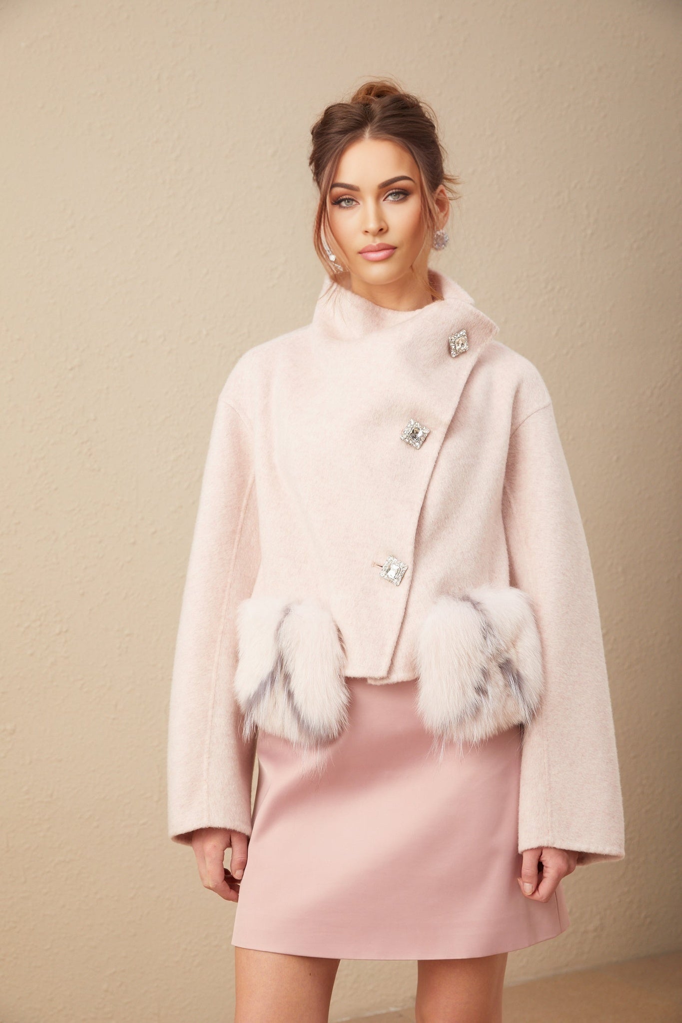 Woman wearing short pink coat with diagonal button placket and collar standing against neutral background