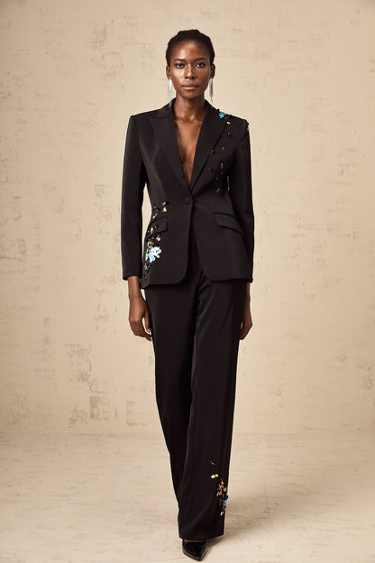 A woman wearing a black sequined blazer and matching trousers standing confidently against a plain background