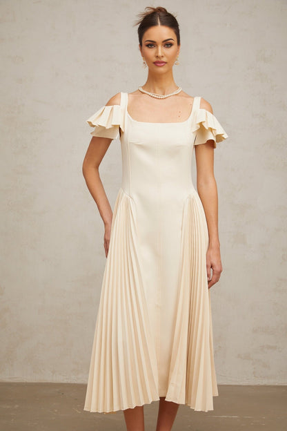 Woman wearing beige pleated midi dress with flared skirt and neutral tones standing in elegant pose