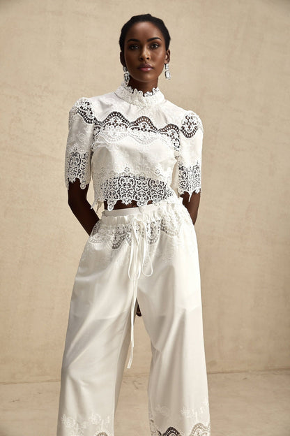Woman wearing white lace trim cropped top and matching trousers with cutout details Raphaelle matching set