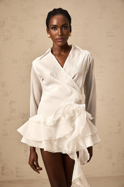 Young woman wearing a white semi sheer mini dress with floral pattern and ruffled details standing in a natural outdoor setting