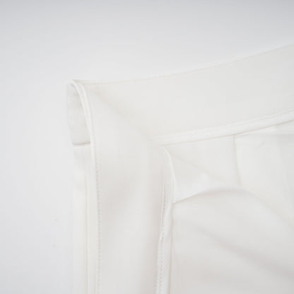 Woman wearing white creased top and matching trousers set standing against plain background