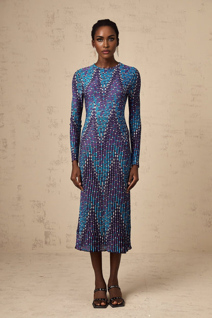 Young woman wearing a blue and white zigzag pattern knitted midi dress with long sleeves standing against a plain background