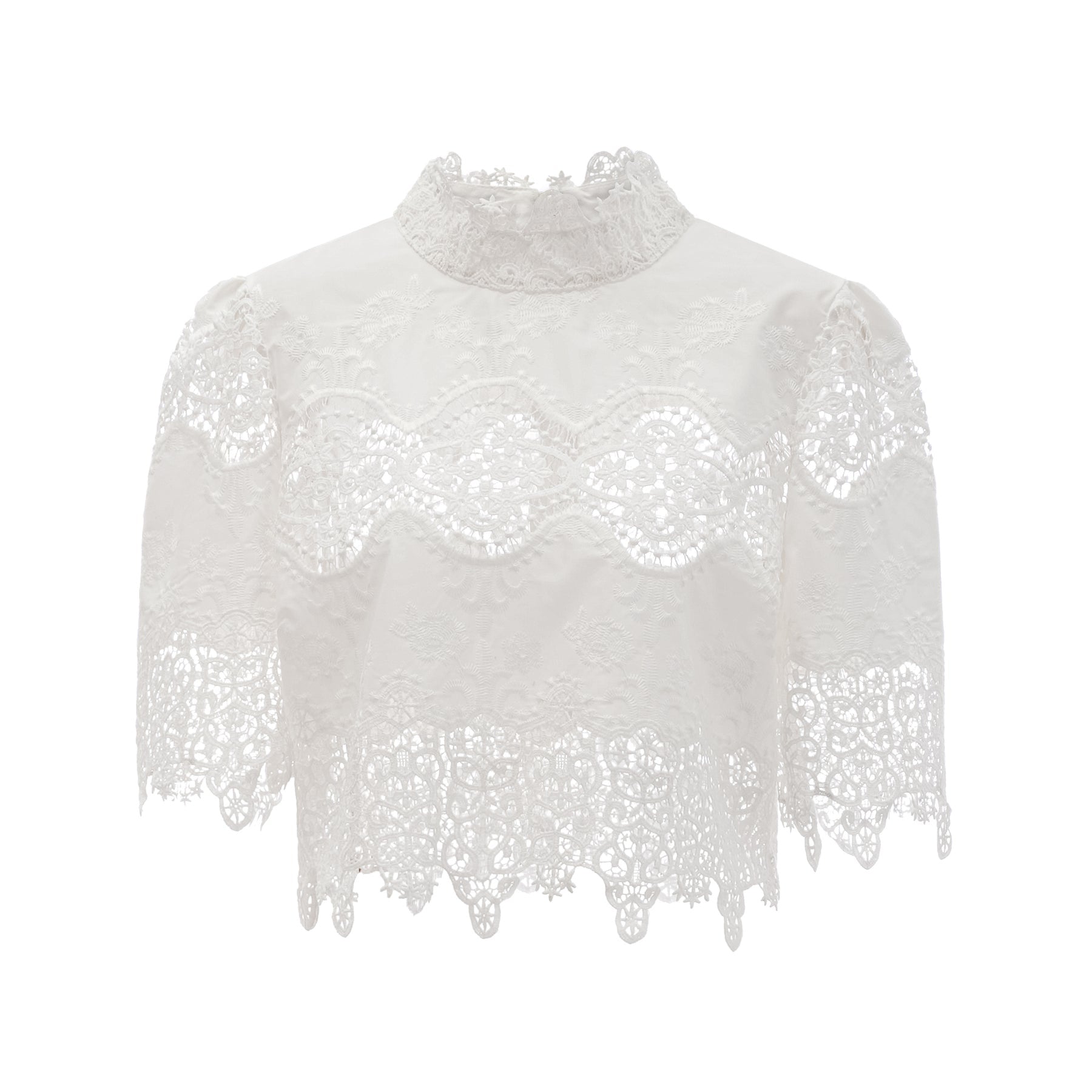 Woman wearing white lace trim cropped top and matching trousers with cutout details standing against plain background