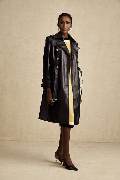 A black leather coat with double breasted front and belt at the waist worn by a model named Camille