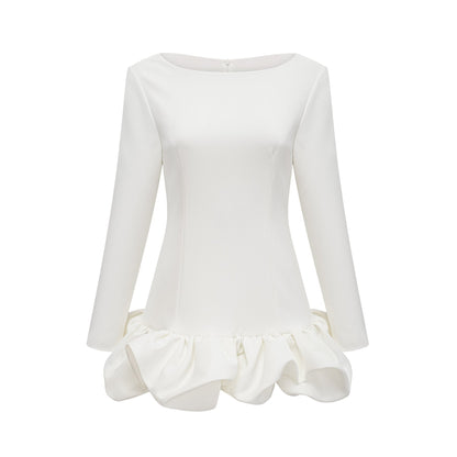 Young woman wearing a white mini dress with a bubble skirt and short sleeves standing against a plain background