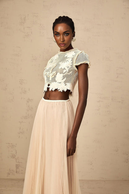 Woman wearing a matching set consisting of a light colored top and skirt with floral applique details in neutral tones