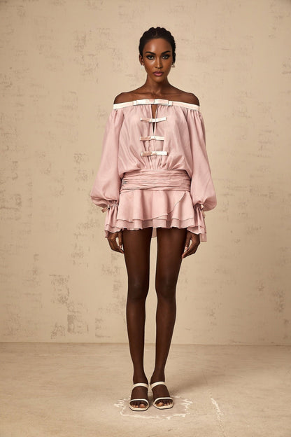 Young woman wearing a pink offshoulder mini dress with bow detail and ruffled hem