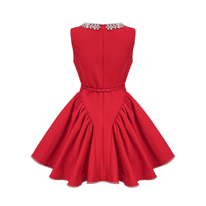 Young woman wearing a red pleated mini dress with embellishments standing in front of a plain background