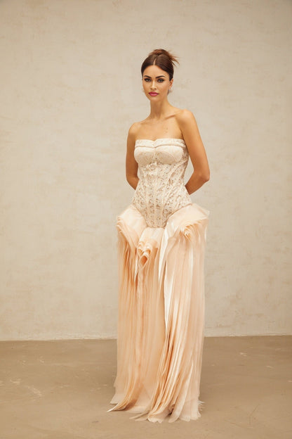 A woman wearing a long neutral colored maxi dress with lace details and corset style bodice layered over a full skirt