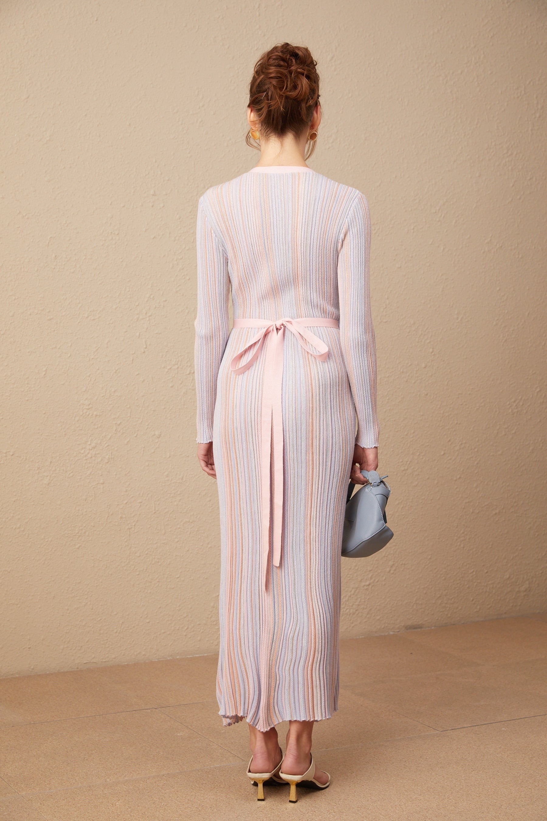 A woman wearing a pleated knit midi dress with a V neckline in a soft color standing against a plain background