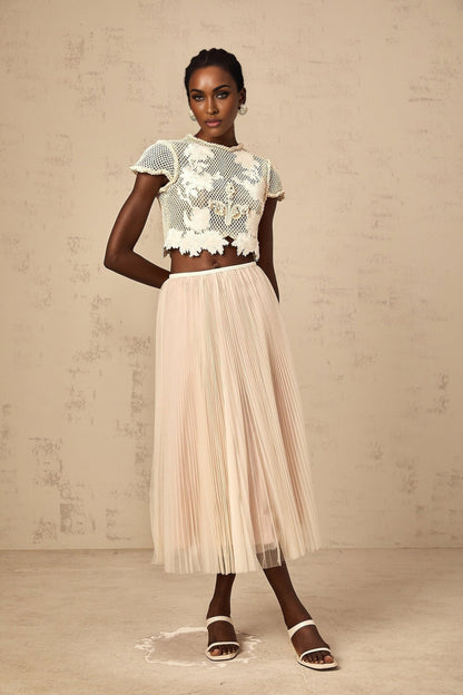 Woman wearing a neutral colored matching top and skirt set with floral applique details