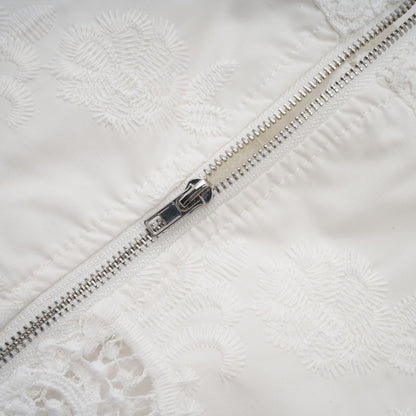 A woman wearing a matching set consisting of a white lace trim cropped top with cutout details and matching white trousers