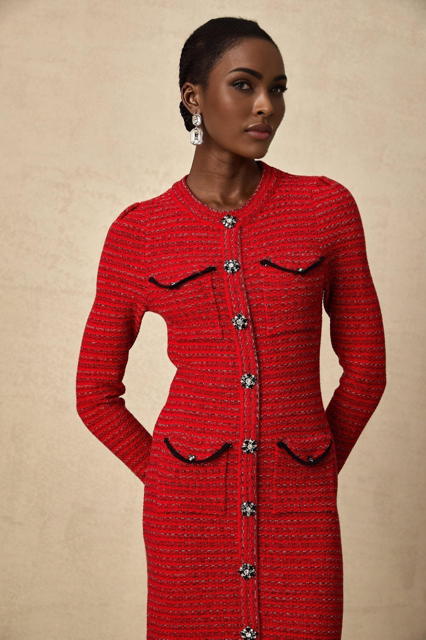 A woman wearing a red knitted midi dress with embellishments standing in a relaxed pose