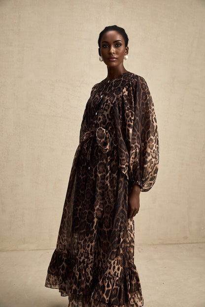 A woman wearing a leopard print midi dress with a single breasted design and long sleeves standing in a neutral pose