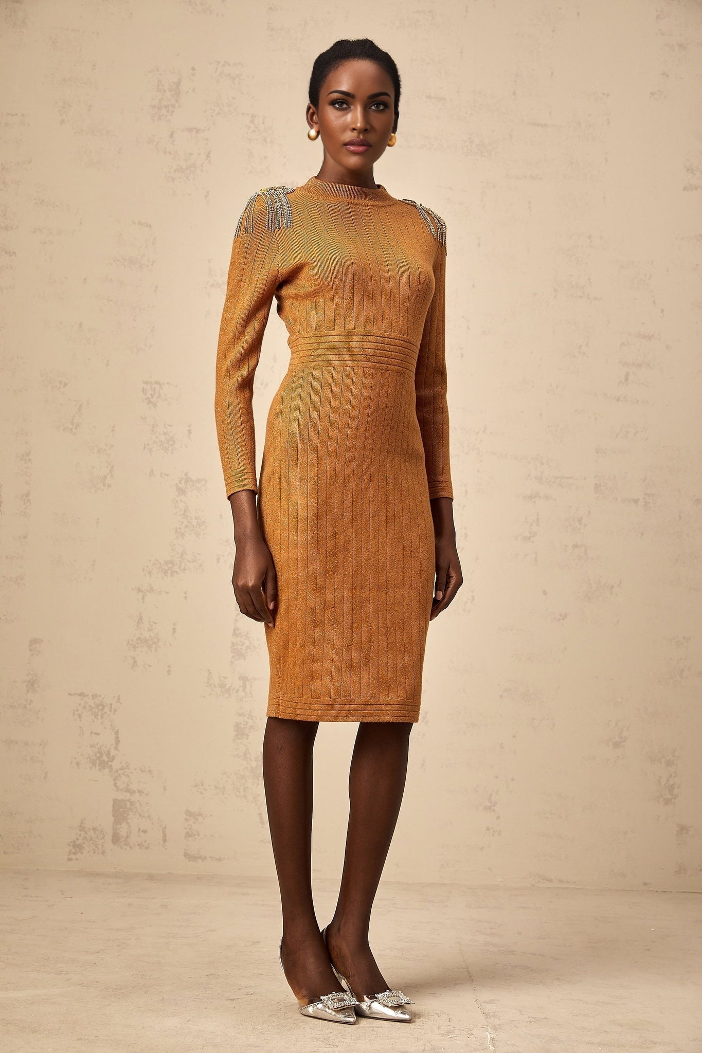 A woman wearing a black ribbed knit midi dress with epaulet details on the shoulders The dress has a fitted silhouette and falls to mid calf length
