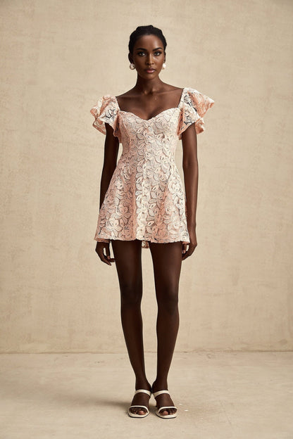 Young woman wearing a pink mini dress with flutter sleeves and lace detailing standing in a relaxed pose against a plain background