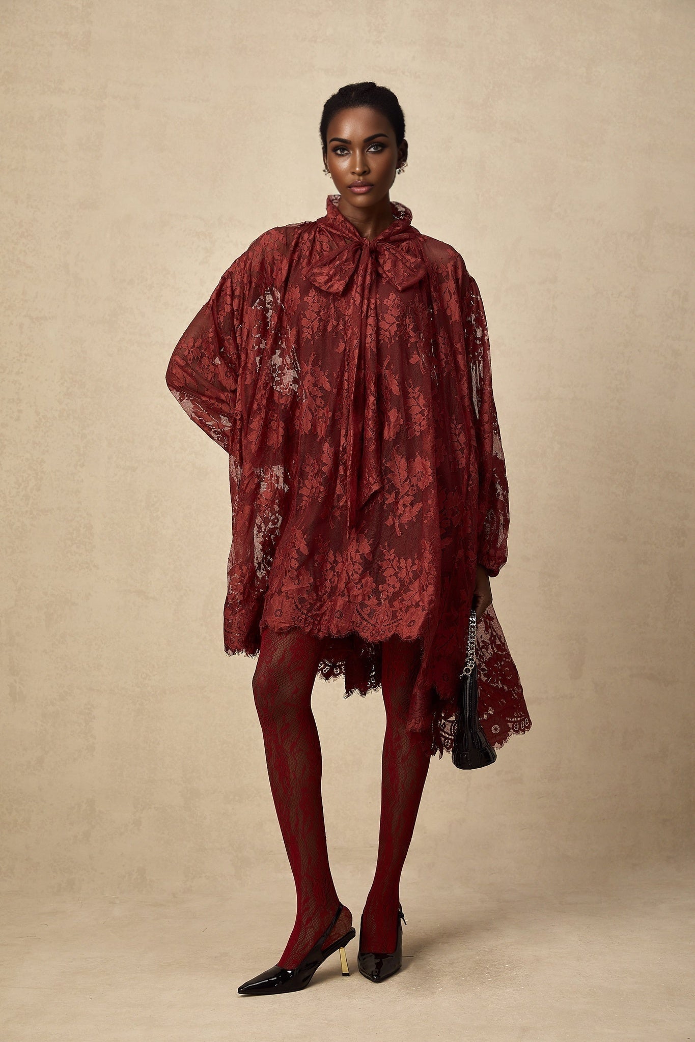 A woman wearing a red oversized dress made of chantilly lace standing in a relaxed pose