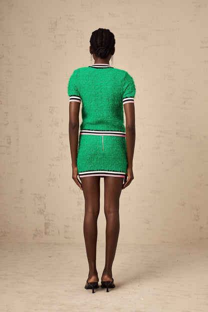 Woman wearing a green knitted top and matching skirt set standing against plain background