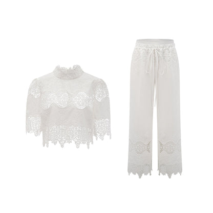 Woman wearing white lace trim cropped top and matching trousers set featuring cutout details