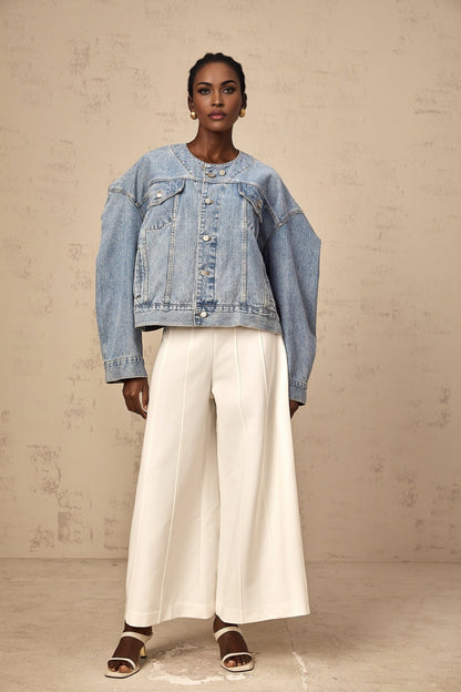 Woman wearing a light blue collarless denim jacket with front pockets and button closure