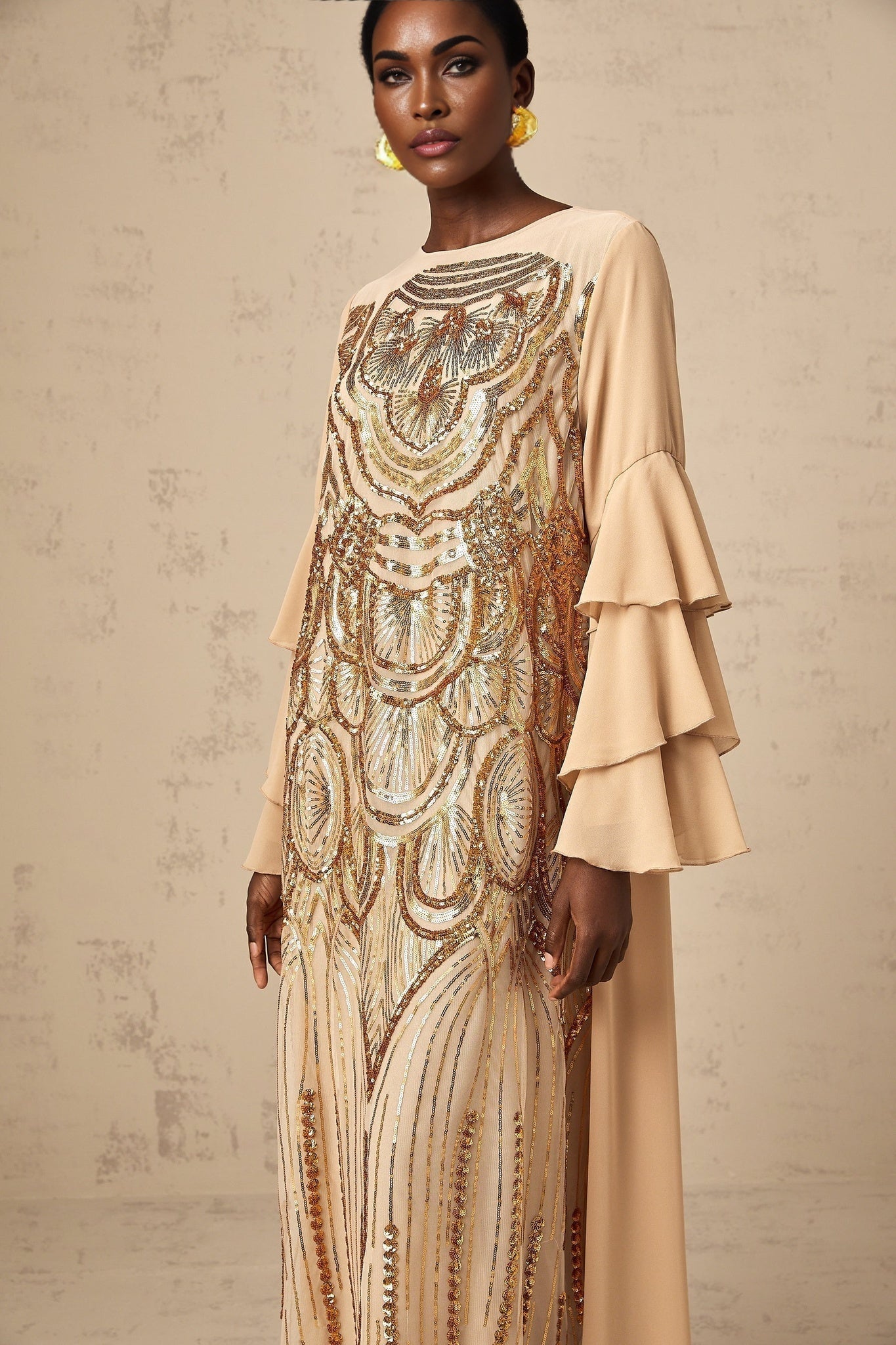 Woman wearing long sequined tulle dress with ruffle sleeves and flowing maxi skirt in elegant pose