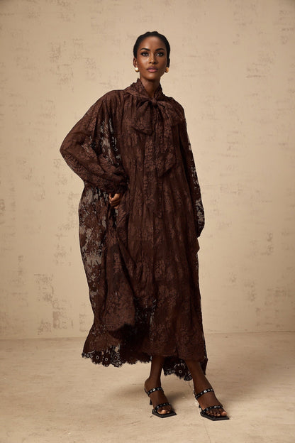 A woman wearing a brown lace midi dress with a flared skirt and delicate chantilly lace pattern The dress has a fitted bodice and falls to mid calf length