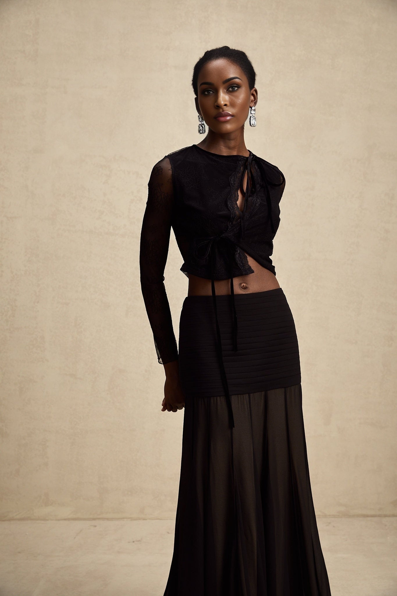 A black cropped top with sheer lace trim worn by a model against a plain background