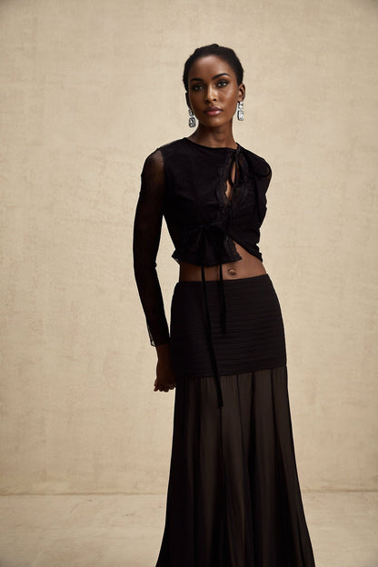 A black cropped top with sheer lace trim worn by a model against a plain background