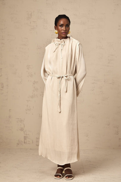 A woman wearing a light colored tulle midi dress with a self tie waist standing in a neutral background