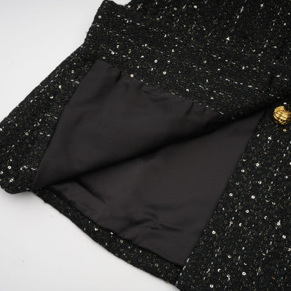 A black mini dress featuring a tweed fabric with sequin panels named Audrey combining classic and glamorous elements in a short silhouette