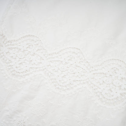 Woman wearing a matching set of white lace trim cropped top and trousers with cutout details