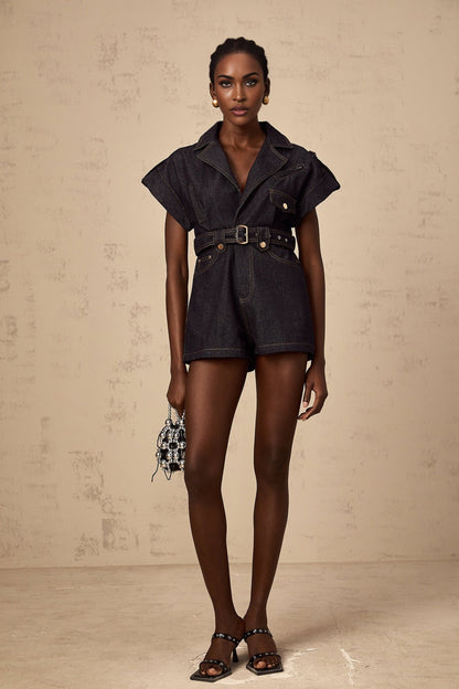 Woman wearing light blue denim playsuit with wide belt cinching the waist short sleeves and relaxed fit