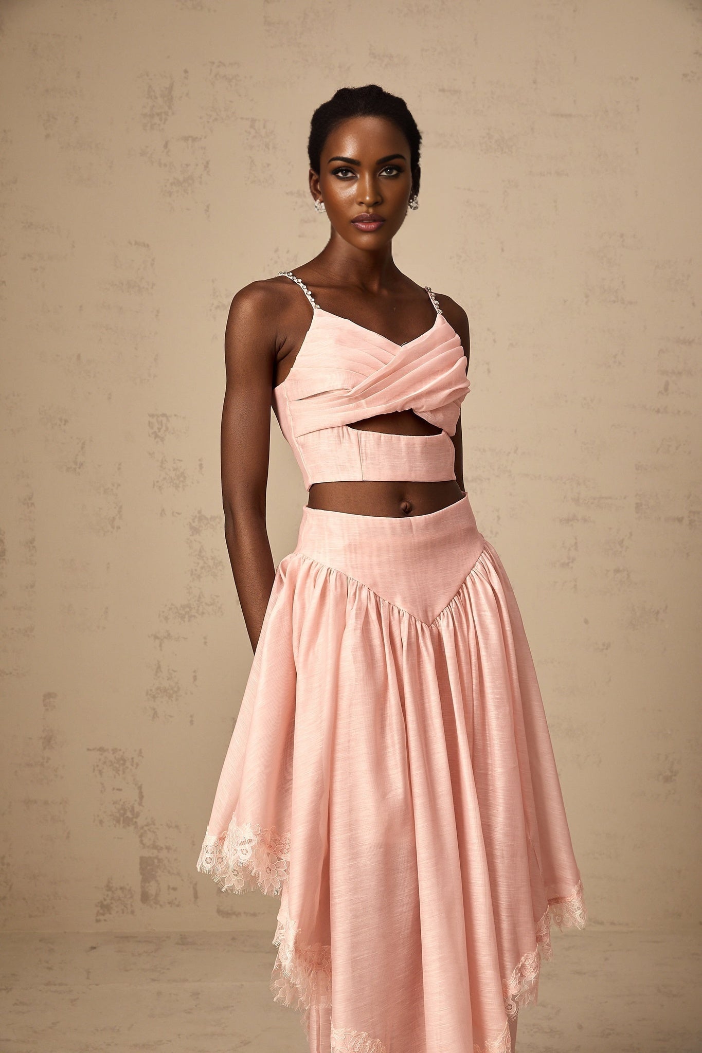 A woman wearing a pink matching set consisting of an asymmetric ruffled top and skirt The top has one shoulder and the skirt features ruffles The outfit is called Tamara and has a feminine and stylish appearance